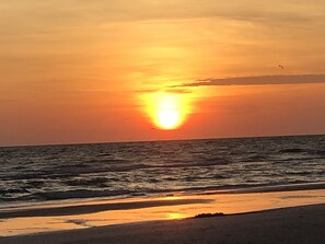 A sunset over the ocean with a beach in the foreground.