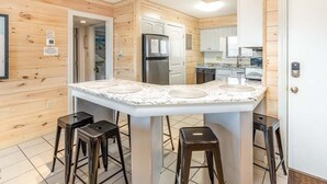 A modern kitchen with a central island, bar stools, wooden paneling, and built-in appliances. - Lighthouse Point 30C | Ocean View Condo, Pools! (Tybee Island)