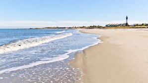 A beach with a lighthouse in the distance, sandy shore, and calm sea. - Lighthouse Point 30C | Ocean View Condo, Pools! (Tybee Island)