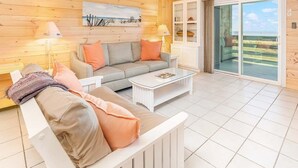 A cozy living room with a sofa, coffee table, and a sliding glass door leading to a balcony. - Lighthouse Point 30C | Ocean View Condo, Pools! (Tybee Island)