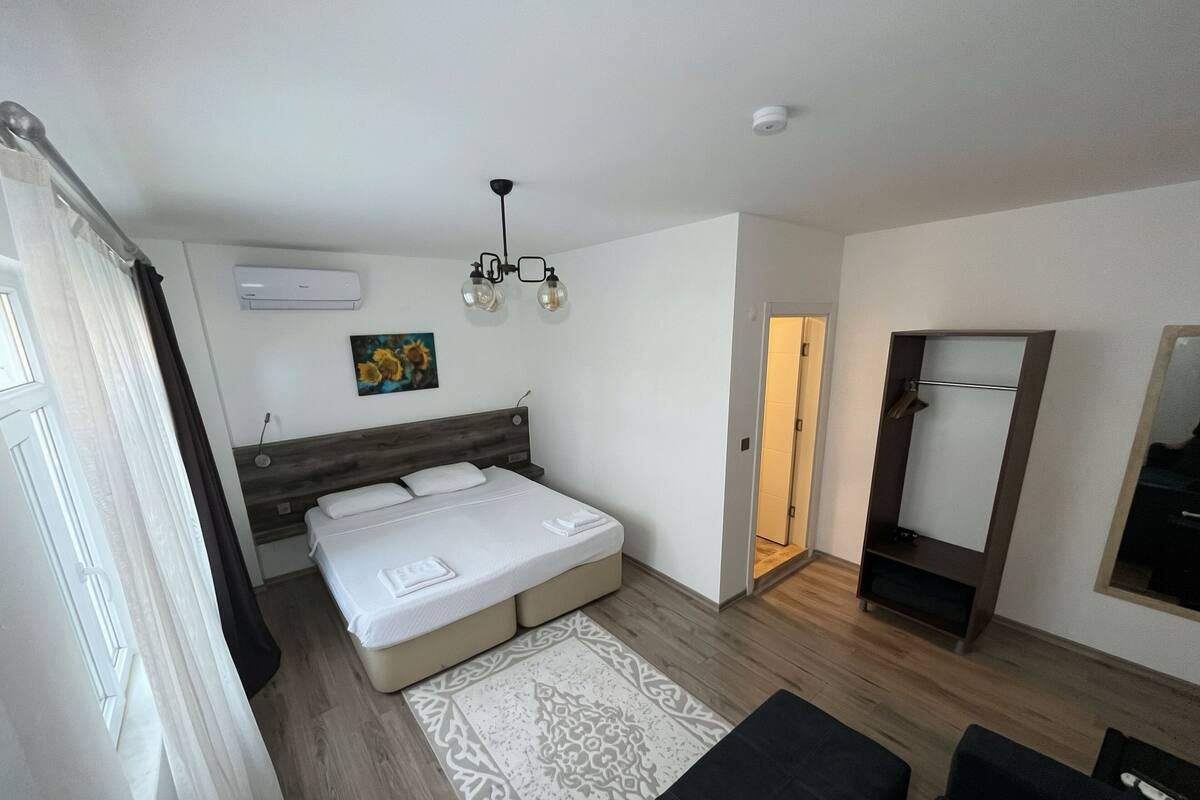 A bedroom with a bed, a bedside table, a mirror, a door, and a light fixture.