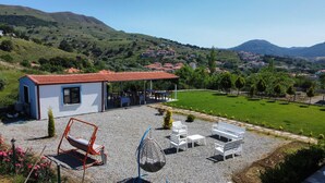 A house with a patio, outdoor seating, and a view of a green valley and hills. - Parli Hotel (Gökçeada)