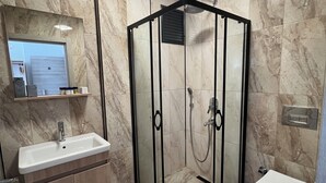 A modern bathroom with a glass-enclosed shower, a sink, and a toilet. - Parli Hotel (Gökçeada)