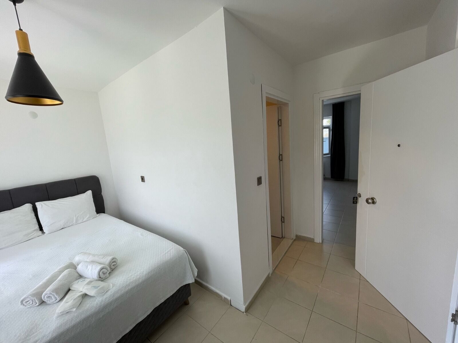A bedroom with a bed, a bedside table, and a hanging light fixture.