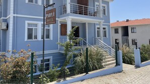 A two-story hotel with a balcony on the upper floor, a sign indicating it is a hotel, and a gated entrance with plants. - Parli Hotel (Gökçeada)