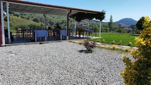 An outdoor seating area with tables and chairs, a gravel ground, and a view of a hilly landscape with buildings in the distance.