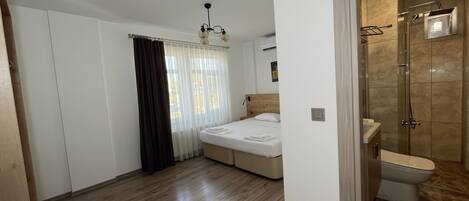 A bedroom with a bed, a shower, and a window with curtains.