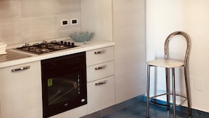 A modern kitchen with white cabinets, a black dishwasher, a gas stove, and a stainless steel chair. - APARTMENT IN VILLA (SANGINETO)