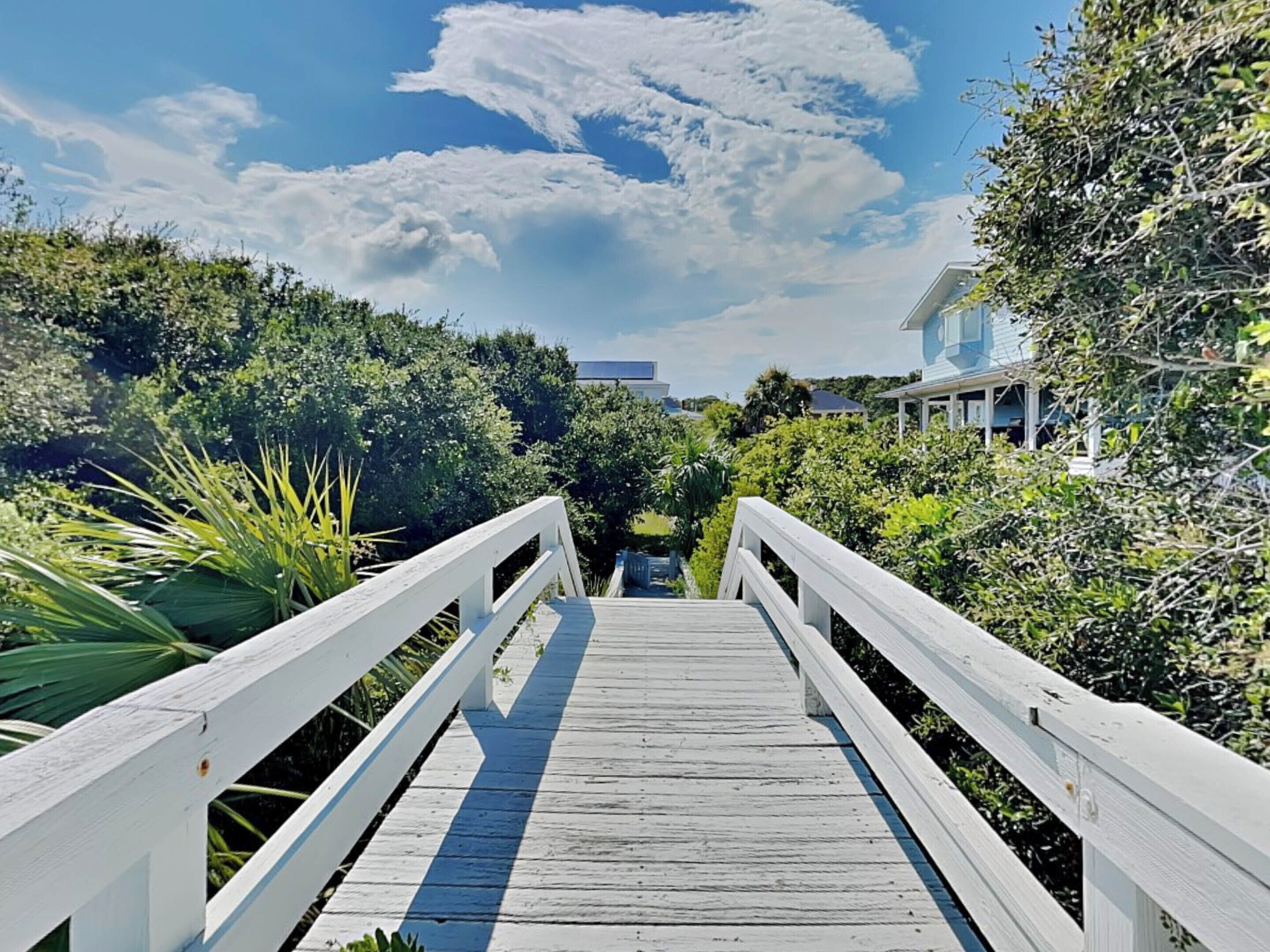 En træpromenade der fører til en bygning omgivet af frodig vegetation.