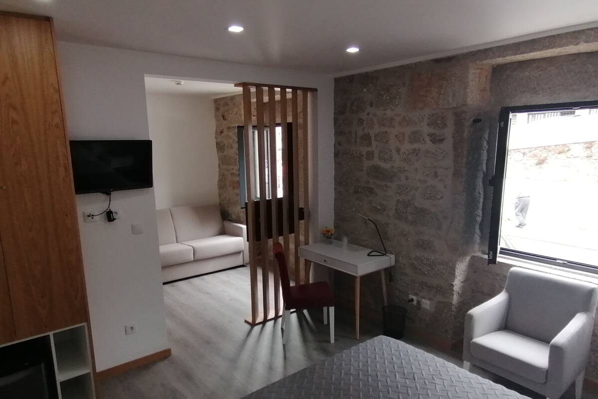 Moderni hotellihuone, jossa on sohva, työpöytä, tuoli ja televisio.
