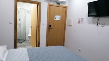 A hotel room with a bed, a shower area, and a mounted TV.