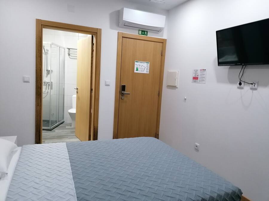 A hotel room with a bed, a shower area, and a mounted TV.