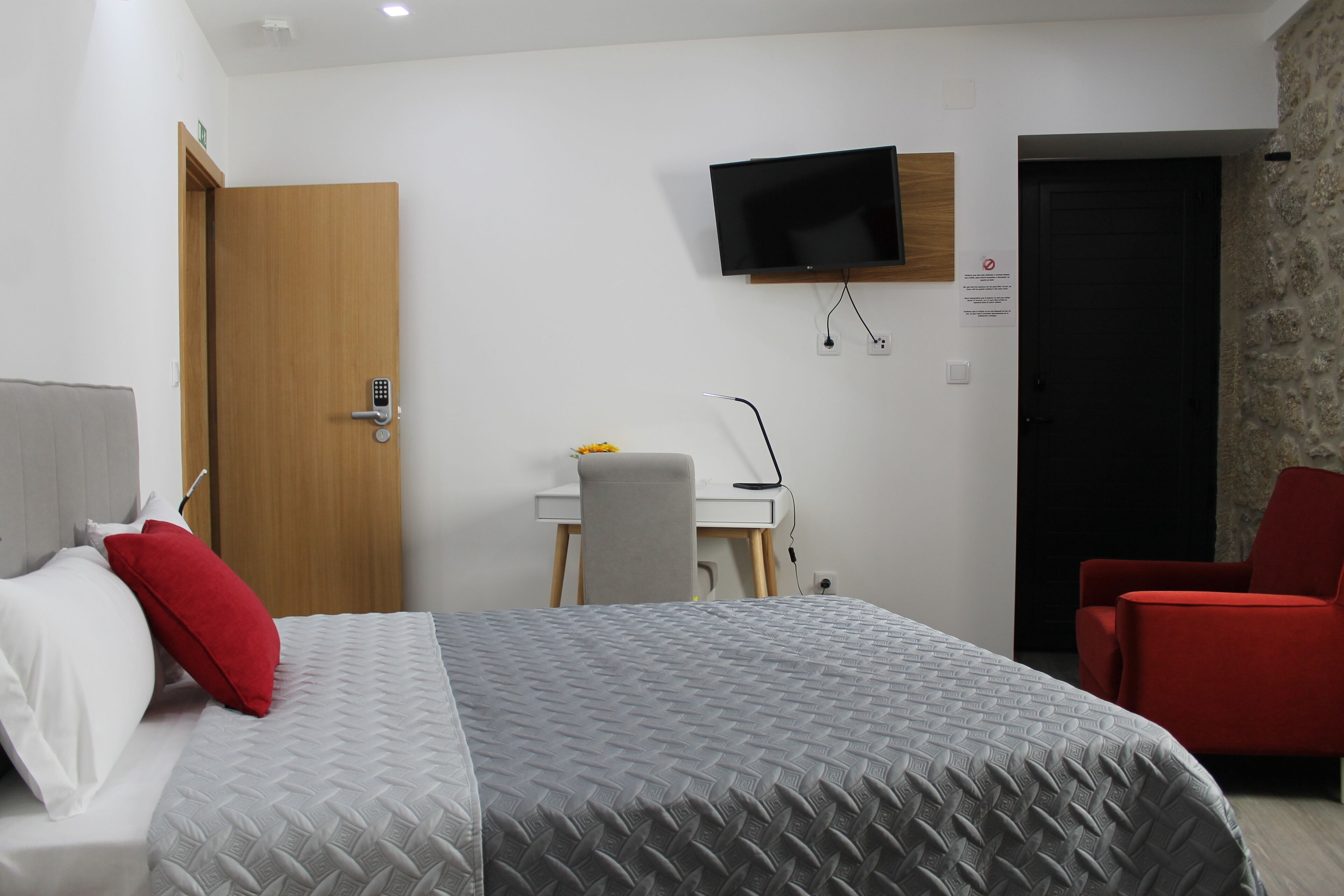 Hotellihuone, jossa on sänky, työpöytä, televisio ja punainen tuoli.