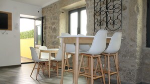 A dining area with a wooden table and white chairs, a stone wall, and a view of greenery outside.