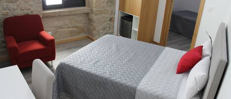 Un dormitorio con una cama, una silla roja, una mesita y una ventana.
