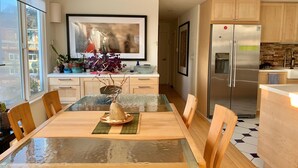 Une cuisine moderne avec des meubles en bois, un réfrigérateur en acier inoxydable et un coin repas comprenant une table et des chaises en verre.