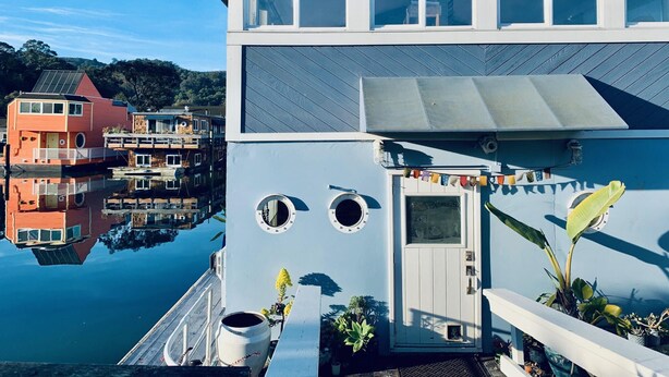 Une maison située au bord de l’eau, dotée d’un quai, de grandes fenêtres et d’une porte avec un petit vitrage.