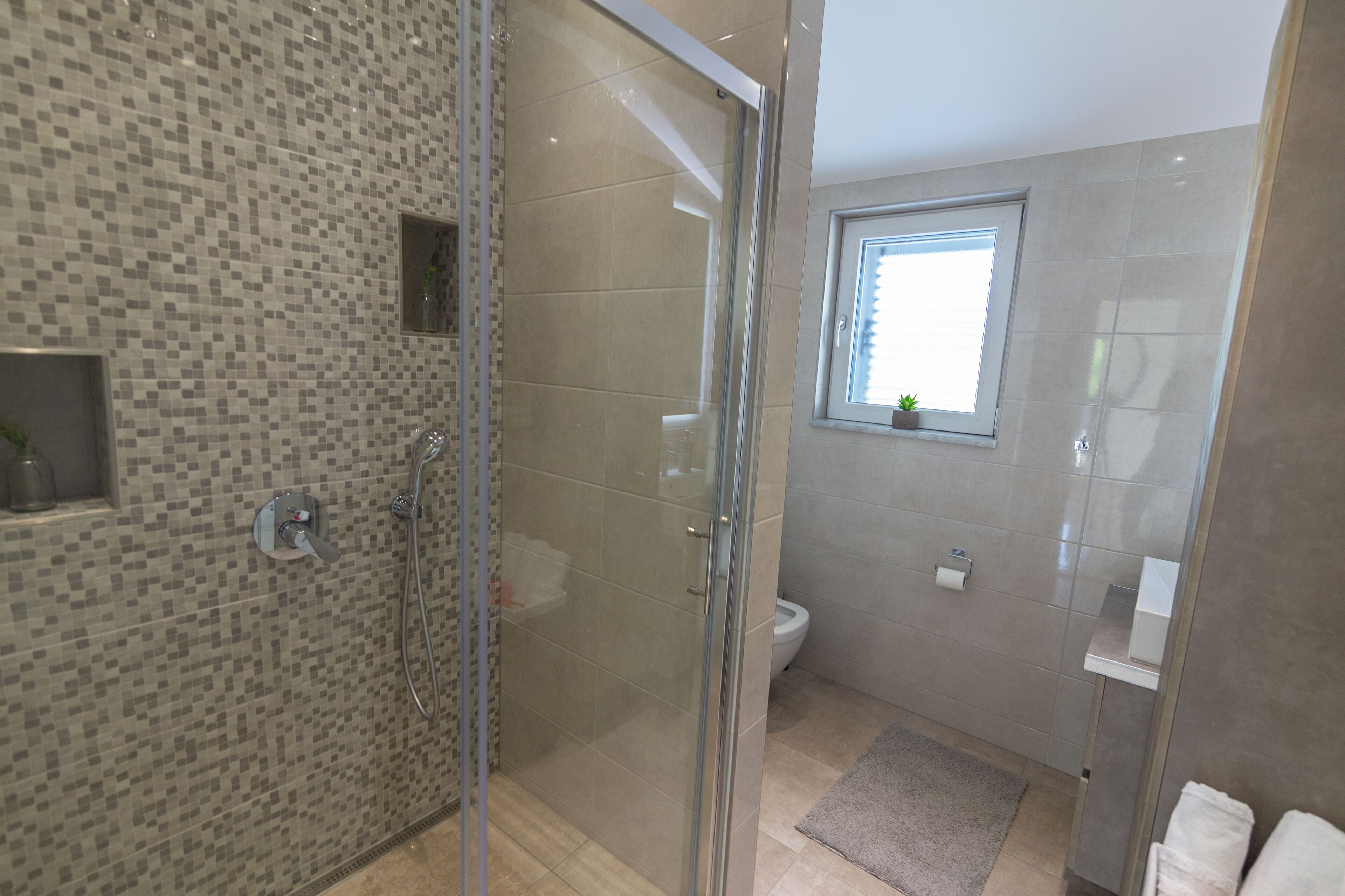 Une salle de bain moderne avec une douche à l’italienne en verre, des toilettes et une petite fenêtre.