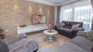 Un salon moderne avec un mur en pierre, un grand téléviseur à écran plat, un canapé foncé, une table basse ronde et une plante en pot.