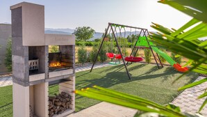 Un jardin avec un barbecue, une balançoire et une vue sur les montagnes.