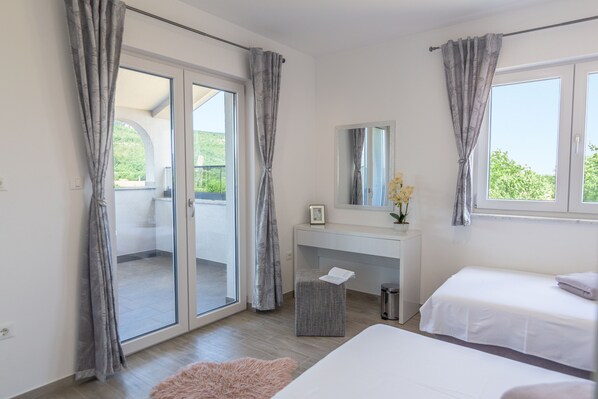 Une chambre avec une porte-fenêtre coulissante donnant sur un balcon, un petit bureau avec un miroir et deux lits.
