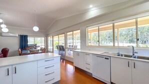 A modern kitchen with white cabinetry, a central island, a built-in dishwasher, and large windows offering views of the outdoors.