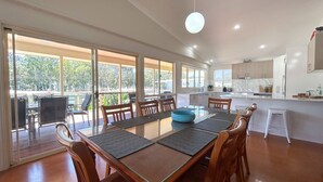 A modern kitchen with white cabinets, a large island, and a dining area with a glass table and wooden chairs.