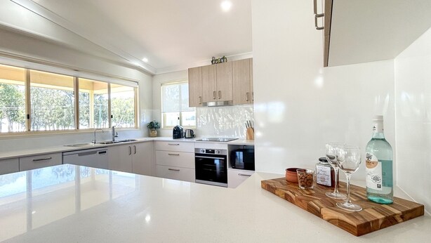 A modern kitchen with a large island, built-in appliances, and a wooden countertop with a bottle and glasses.