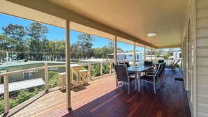 A covered outdoor deck with wooden flooring, metal railings, and a table with chairs.