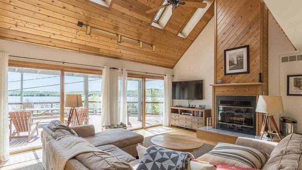 Een ruime woonkamer met een hoge plafond, houten balken, een open haard, een televisie en een groot raam met uitzicht op een prachtig landschap.