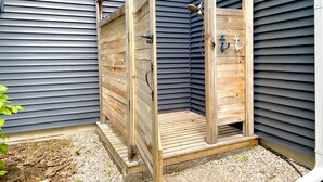 Een houten douchecabine buiten, met een metalen deur en douchekop.