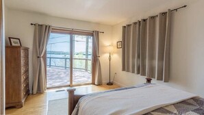 Een slaapkamer met een bed, een dressoir, een vloerlamp en uitzicht op een balkon.