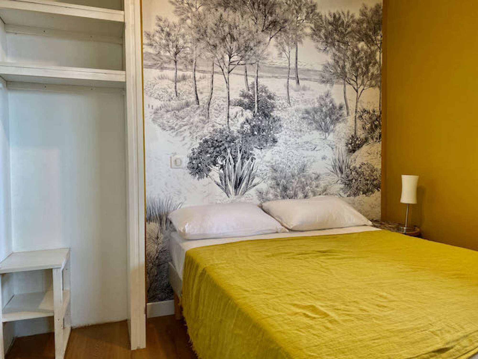 Un dormitorio con cama, mesita de noche, lámpara y armario.