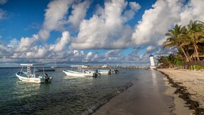 Une plage avec des bateaux, un phare et des palmiers.