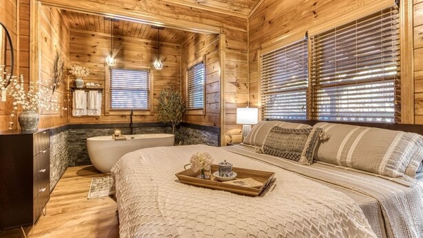 Un dormitorio de estilo cabaña de troncos con una cama grande, un aparador de madera, un tocador y una ba ñera.