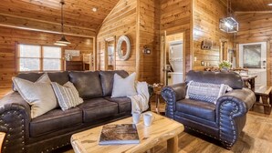 Interior acogedor de una cabaña de troncos con un sofá de cuero, un sillón a juego y una mesa de centro de madera.