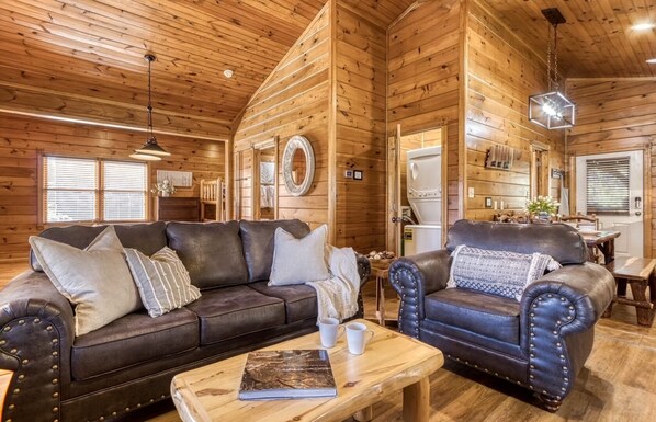 A cozy log cabin interior with a leather sofa, a matching armchair, and a wooden coffee table. - Luxurious cabin with an amazing wooded view (Gatlinburg)