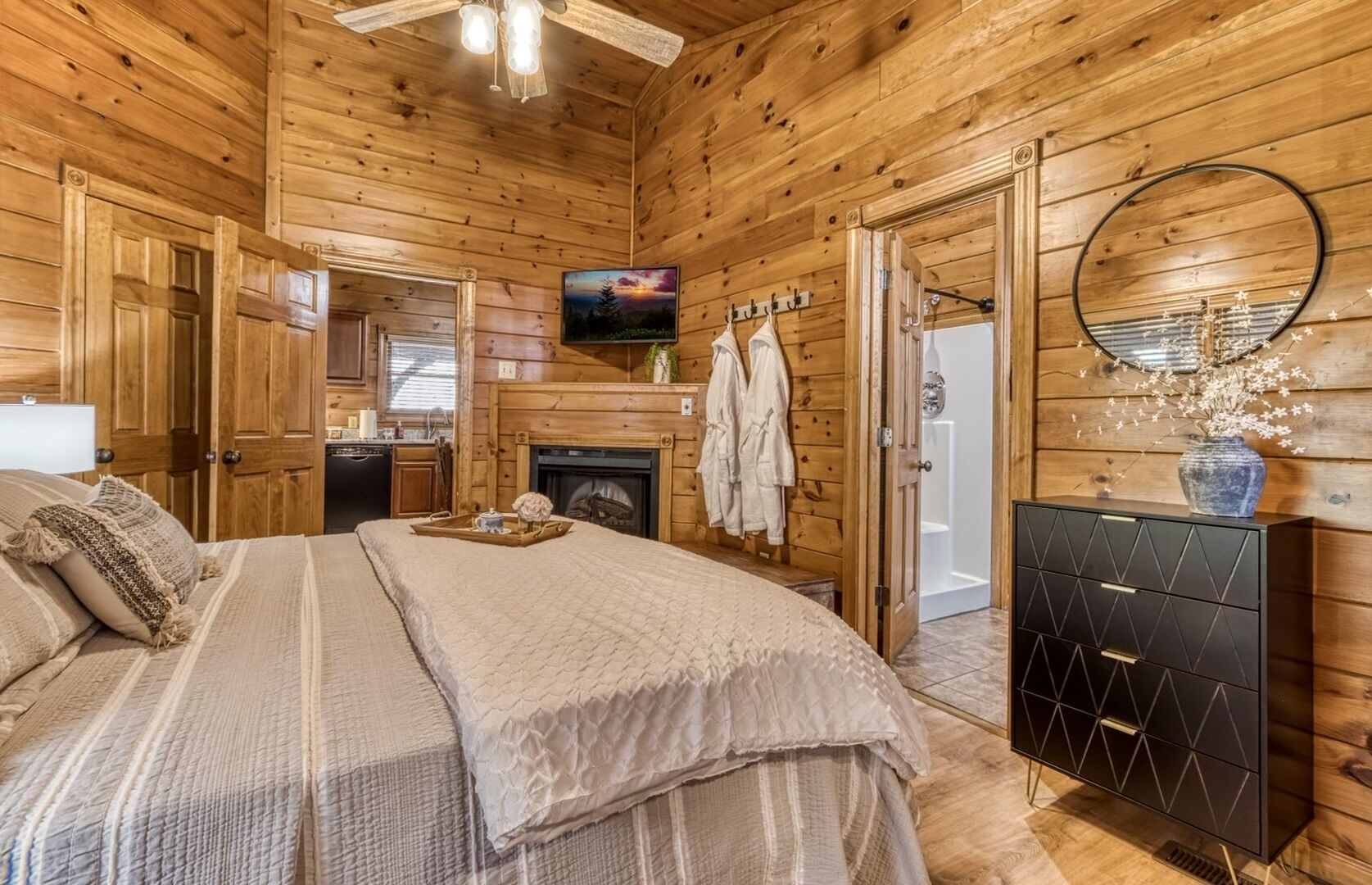 A cozy wooden cabin bedroom with a bed, a dresser, a fireplace, and a television.