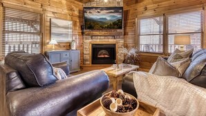 Interior acogedor de una cabaña con chimenea, sofás de cuero y una televisión.