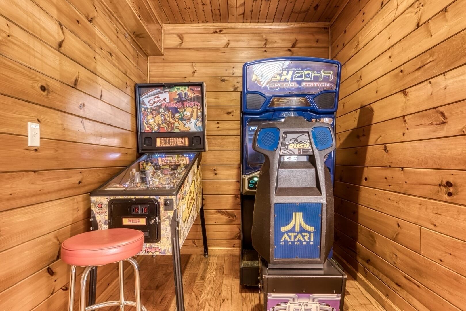 A wooden room with two arcade machines, one labeled "The Simpsons" and the other "Rush 2049 Special Edition".