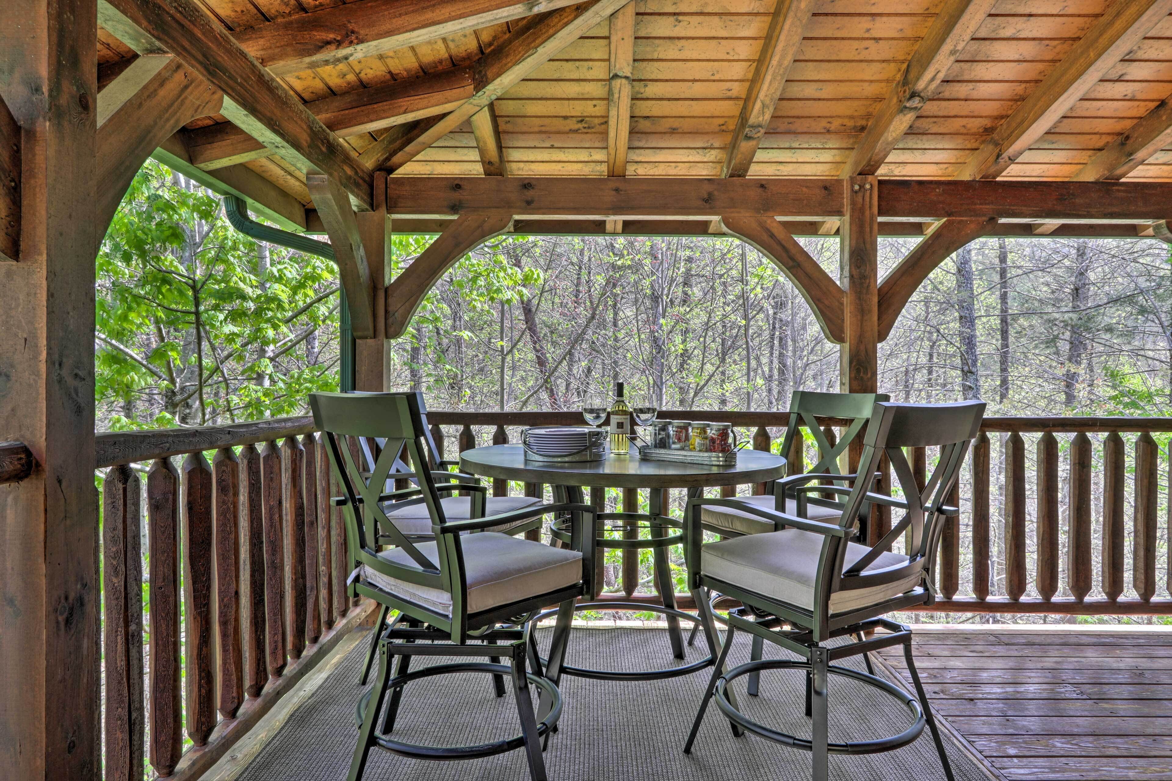 Un espace extérieur abrité, avec une table et des chaises, entouré d’une terrasse en bois et offrant une vue sur une forêt.