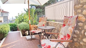 En udendørs terrasse med et rundt bord og to stole, en hvid parasol samt en stenvæg.