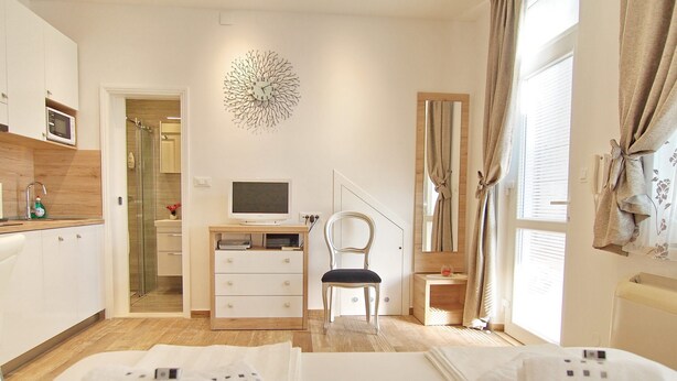 Et moderne hotelværelse med seng, skrivebord med computer, stol, fjernsyn og et badeværelse, der kan ses gennem en åben dør.