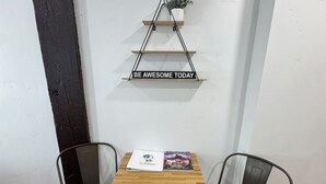 Un piccolo tavolo di legno con due sedie metalliche, una targa bianca con la scritta “BE AWESOME TODAY” e una pianta su una mensola a parete.