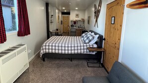 Una camera da letto con un letto, una ventola a soffitto, un termosifone, un divano e vista su cucina e bagno.
