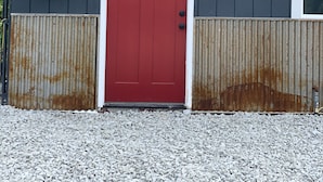 Un edificio con una porta rossa con la lettera 'E', una finestra e un serbatoio d'acqua a sinistra.