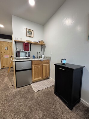 A compact kitchen with a refrigerator, microwave, sink, and a small black cabinet.