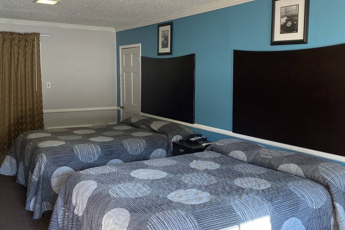 A hotel room with two beds, a large window, a door, and a framed picture on the wall.