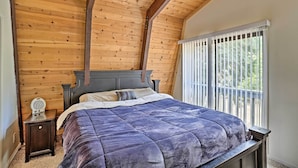 Un dormitorio con techo de madera, una cama con colcha azul, una mesita de noche y una ventana con persianas.