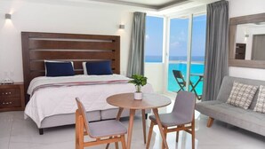 A hotel room with a large bed, a round table with two chairs, a sofa, and a balcony with a view of the ocean. - Direct Beachfront Paradise: Studio w/ Balcony + Resort Amenities (Cancún)
